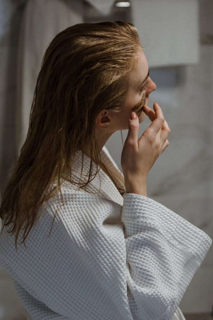 young woman in bathrobe applying cosmetic mask on face